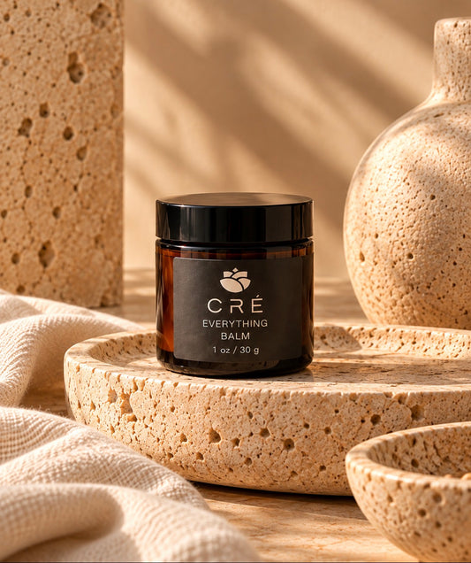 Crè Everything Balm in an amber jar with black lid, styled on warm neutral stone.